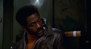 Movie still from “Shaft” (1971), directed by Gordon Parks – A man in a brown leather jacket looking down at his face; Close Up shot, Over the shoulder angle
