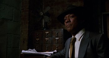 Movie still from “Shaft” (1971), directed by Gordon Parks – A man in a suit and a hat holding papers in a room; Close Up shot, Low angle