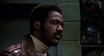 Movie still from “Shaft” (1971), directed by Gordon Parks – A black man with a beard and a brown jacket looking to his left; Close Up shot, Low angle
