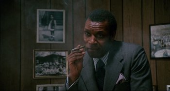 Movie still from “Shaft” (1971), directed by Gordon Parks – A man in a suit smoking a cigarette in a room; Close Up shot, Low angle