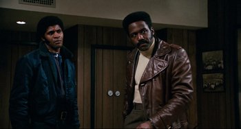 Movie still from “Shaft” (1971), directed by Gordon Parks – A man in a brown leather jacket standing next to another man; Medium shot, Low angle