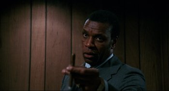 Movie still from “Shaft” (1971), directed by Gordon Parks – A man in a suit and tie holding a wooden stick; Close Up shot, Low angle