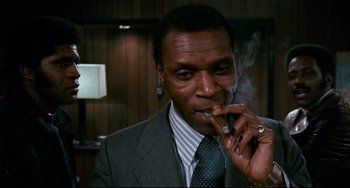 Movie still from “Shaft” (1971), directed by Gordon Parks – A man in a gray suit smoking a cigarette; Close Up shot, Low angle