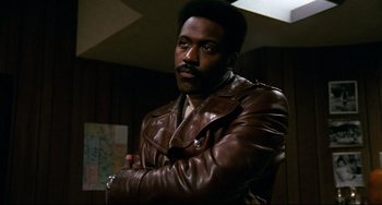 Movie still from “Shaft” (1971), directed by Gordon Parks – A man in a brown leather jacket posing for a picture; Close Up shot, Low angle
