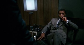 Movie still from “Shaft” (1971), directed by Gordon Parks – A man in a suit sitting in a chair in front of a lamp; Medium shot, Low angle