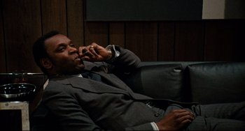 Movie still from “Shaft” (1971), directed by Gordon Parks – A man sitting on a couch while talking on a cell phone; Medium shot, Low angle