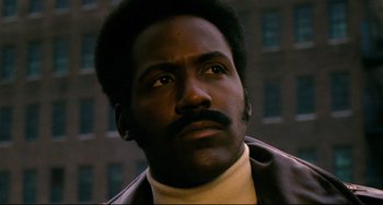 Movie still from “Shaft” (1971), directed by Gordon Parks – A person wearing a jacket with a building in the background; Close Up shot, Low angle