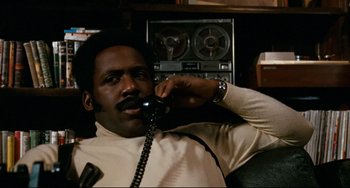 Movie still from “Shaft” (1971), directed by Gordon Parks – A man talking on a phone while sitting in a chair; Close Up shot, Low angle