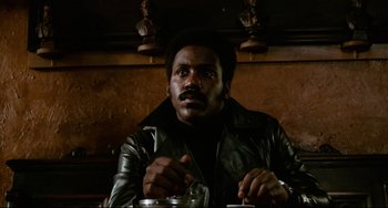 Movie still from “Shaft” (1971), directed by Gordon Parks – A man sitting at a table in a leather jacket; Close Up shot, Low angle