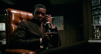 Movie still from “Shaft” (1971), directed by Gordon Parks – A man sitting in a chair talking on a phone; Medium shot, Low angle