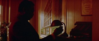 Movie still from “Shaft's Big Score!” (1972), directed by Gordon Parks – A person holding a lamp in front of a window; Medium shot, Low angle