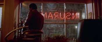 Movie still from “Shaft's Big Score!” (1972), directed by Gordon Parks – A man sitting in front of a window with a neon sign; Medium shot, Over the shoulder angle