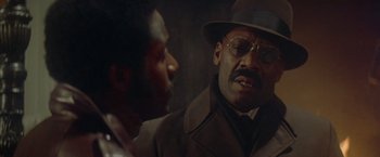 Movie still from “Shaft's Big Score!” (1972), directed by Gordon Parks – A man in a hat and glasses talking to another man in a suit; Close Up shot, Over the shoulder angle