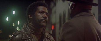 Movie still from “Shaft's Big Score!” (1972), directed by Gordon Parks – A man wearing a brown leather jacket talking to another man; Close Up shot, Over the shoulder angle
