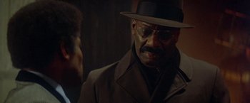 Movie still from “Shaft's Big Score!” (1972), directed by Gordon Parks – An older man wearing a hat and glasses; Close Up shot, Over the shoulder angle