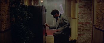 Movie still from “Shaft's Big Score!” (1972), directed by Gordon Parks – A man sitting in front of an open cabinet; Medium shot, Low angle