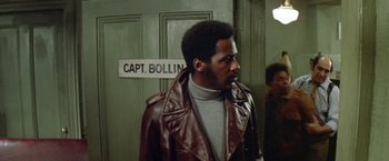Movie still from “Shaft's Big Score!” (1972), directed by Gordon Parks – A man in a brown leather jacket standing in front of a door; Medium shot, Low angle