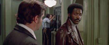 Movie still from “Shaft's Big Score!” (1972), directed by Gordon Parks – A man in a brown leather jacket standing in front of another man in a suit; Medium shot, Over the shoulder angle
