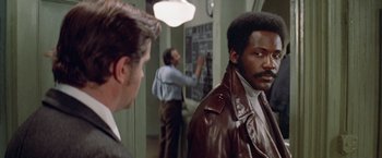 Movie still from “Shaft's Big Score!” (1972), directed by Gordon Parks – A man in a brown leather jacket standing next to another man; Close Up shot, Over the shoulder angle