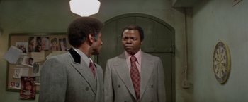 Movie still from “Shaft's Big Score!” (1972), directed by Gordon Parks – A man in a suit and tie looking at himself in the mirror; Medium shot, Low angle