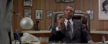 Movie still from “Shaft's Big Score!” (1972), directed by Gordon Parks – A man sitting at a table in a suit and tie; Medium shot, Low angle