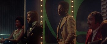 Movie still from “Shaft's Big Score!” (1972), directed by Gordon Parks – A man in a brown suit standing in front of a mirror; Medium shot, Low angle