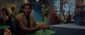 Movie still from “Shaft's Big Score!” (1972), directed by Gordon Parks – A man sitting at a table holding a large knife; Medium shot, Over the shoulder angle