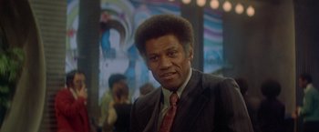 Movie still from “Shaft's Big Score!” (1972), directed by Gordon Parks – A man in a suit and tie in front of a crowd; Close Up shot, Over the shoulder angle