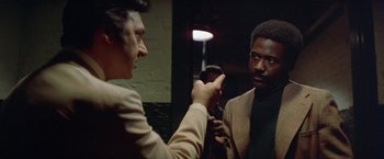 Movie still from “Shaft's Big Score!” (1972), directed by Gordon Parks – Two men are talking to each other in a dark room; Medium shot, Over the shoulder angle
