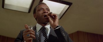 Movie still from “Shaft's Big Score!” (1972), directed by Gordon Parks – A man in a suit smoking a cigar and holding a drink; Close Up shot, Low angle