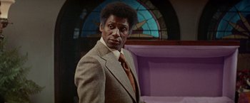 Movie still from “Shaft's Big Score!” (1972), directed by Gordon Parks – A man wearing a suit and tie in front of a stained glass window; Medium shot, Low angle