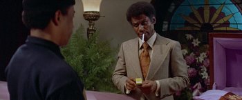 Movie still from “Shaft's Big Score!” (1972), directed by Gordon Parks – A man in a suit and tie smoking a cigarette; Close Up shot, Over the shoulder angle