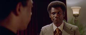 Movie still from “Shaft's Big Score!” (1972), directed by Gordon Parks – A man in a suit and tie looking into a mirror; Close Up shot, Over the shoulder angle