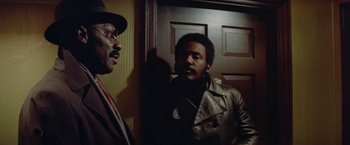 Movie still from “Shaft's Big Score!” (1972), directed by Gordon Parks – Two men standing next to each other near a door; Medium shot, Over the shoulder angle