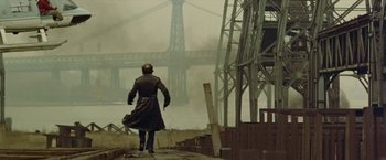 Movie still from “Shaft's Big Score!” (1972), directed by Gordon Parks – A man in a trench coat walking in front of a bridge; Wide shot, Low angle