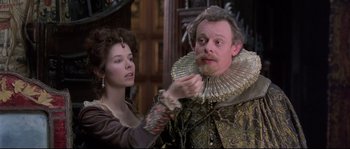 Movie still from “Shakespeare in Love” (1998), directed by John Madden – A man with a beard and a wig is being fitted by a woman; Close Up shot, Over the shoulder angle