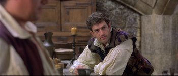 Movie still from “Shakespeare in Love” (1998), directed by John Madden – A man sitting at a table with a candle in the background; Medium shot, Over the shoulder angle