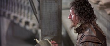 Movie still from “Shakespeare in Love” (1998), directed by John Madden – A man with long hair and a beard is holding a book; Close Up shot, Over the shoulder angle