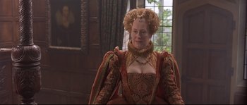 Movie still from “Shakespeare in Love” (1998), directed by John Madden – A woman in a red and gold dress sitting in a chair; Medium shot, Over the shoulder angle