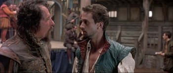 Movie still from “Shakespeare in Love” (1998), directed by John Madden – A man wearing a green and red jacket talking to another man; Medium shot, Over the shoulder angle