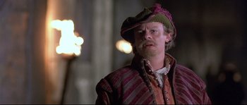 Movie still from “Shakespeare in Love” (1998), directed by John Madden – A man with a beard wearing a hat and a jacket; Close Up shot, Over the shoulder angle