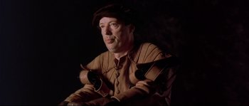 Movie still from “Shakespeare in Love” (1998), directed by John Madden – A man wearing a hat and gloves sitting in a chair; Close Up shot, High angle