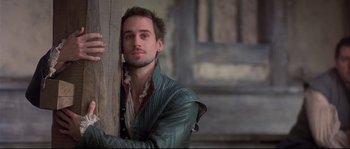 Movie still from “Shakespeare in Love” (1998), directed by John Madden – A man in a green jacket leaning against a wooden post; Close Up shot, Over the shoulder angle