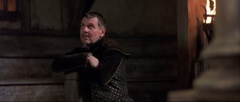 Movie still from “Shakespeare in Love” (1998), directed by John Madden – A man in a black and brown outfit leaning on a wooden post; Medium shot, Low angle
