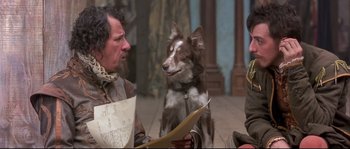 Movie still from “Shakespeare in Love” (1998), directed by John Madden – A man and a dog sitting next to each other on the floor; Medium shot, Over the shoulder angle