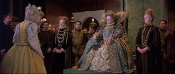 Movie still from “Shakespeare in Love” (1998), directed by John Madden – A group of people standing next to each other in a room; Wide shot, Low angle