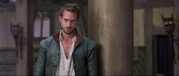 Movie still from “Shakespeare in Love” (1998), directed by John Madden – A man in a medieval outfit standing in front of a wooden wall; Medium shot, Over the shoulder angle
