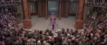 Movie still from “Shakespeare in Love” (1998), directed by John Madden – A crowd of people watching a man in a purple costume; Extreme Wide shot, High angle