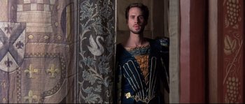 Movie still from “Shakespeare in Love” (1998), directed by John Madden – A man dressed in medieval clothing standing next to a column; Medium shot, Over the shoulder angle