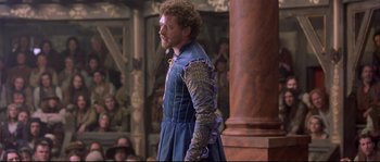 Movie still from “Shakespeare in Love” (1998), directed by John Madden – A man in a blue and gold outfit standing in front of a crowd; Medium shot, Over the shoulder angle